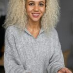 Happy ethnic female with blond curly hair with roasted potato smiling and looking at camera